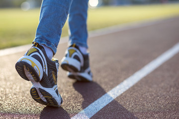 Fototapeta na wymiar Close up of woman feet in sport sneakers and blue jeans on running lane on outdoor sports court.