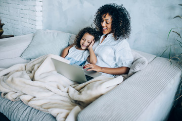Laughing girl with woman using laptop on couch