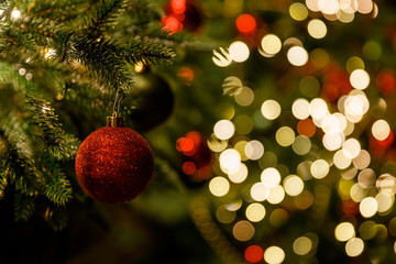 Christmas and New Year interior - blur background: fireplace, lamps, green Christmas tree, brown leather sofa, gifts, candles, moose rocking chair. Lots of lights glowing in the dark.