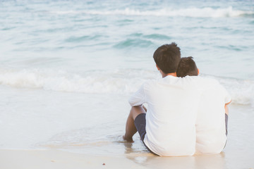 Back view homosexual portrait young asian couple sitting hug together on beach in summer, asia gay going tourism for leisure and relax with romantic and happy in vacation at sea, LGBT legal concept.