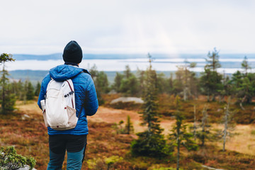 Man traveler in a blue jacket with a backpack hiking in the autumn forest in Finland.