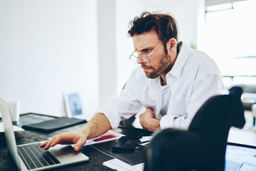 Fototapeta premium Serious male entrepreneur concentrated during remote job searching information on web pages via laptop computer, man freelancer read publication in blog via netbook work from home at desktop.
