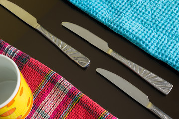 Blue and colored lines table-napkins and cutlery as a still life on dark reflective table. Three...