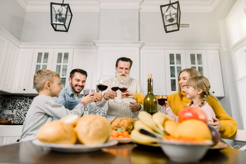 Happy large family sitting at a table at home for Thanksgiving dinner making a toast with glasses of red wine. Grandfather, parents and two children