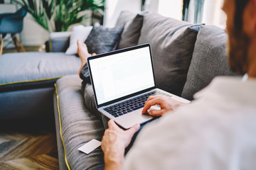 Back view of skilled man taking rest on couch with laptop computer with mock up screen for your internet advertising, male blogger publishing new article on content website using 4g wireless