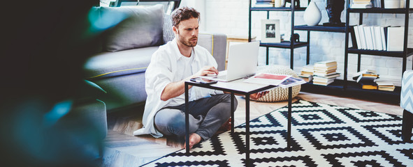Serious caucasian millennial male making online booking via laptop computer sitting in modern...
