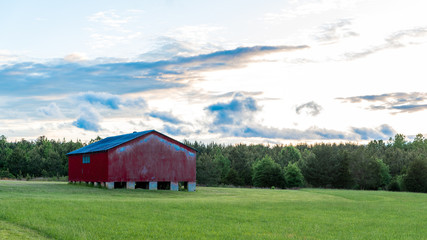Obraz premium Red barn in a field with sky and clouds in the background
