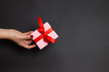 Happy Holidays concept with female hand hold surprise gift with red atlas ribbon on dark...
