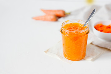 Vegetarian carrot jam or marmalade with orange juice in a glass jar on a white background with copy space for text.Healthy organic vegetable dessert for breakfast.Horizontal orientation