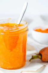 Vegetarian carrot jam or marmalade with orange juice in a glass jar on a white background close-up.Healthy organic vegetable dessert for breakfast.Vertical orientation