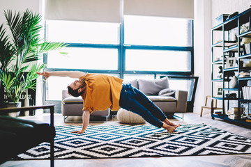 Experienced male lover of yoga in sportive wear stretching hand standing in yoga pose during...