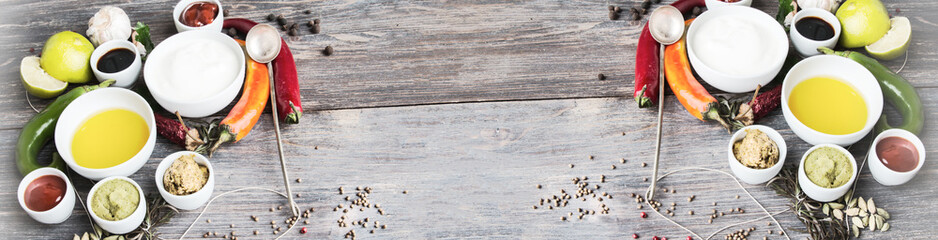 Sauces, spice, herbs, oil, condiments, seeds,cream, vegetables, lime, peppers, dried herbs, bowls, spoon on rustic wooden table. Selective focus.Wide half banner format.