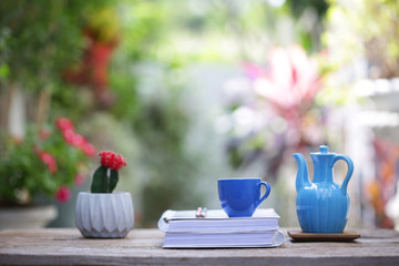 Blue cup with small cactus plant and diary notebook with blue jar on wooden table at outdoor