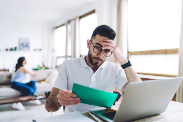 Young man with trendy haircut and thoughtful face looking at green paper
