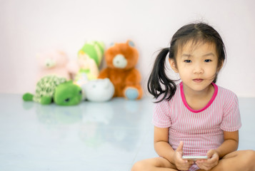 Fototapeta na wymiar an Asian girlThe kindergartener was playing the phone with fun, ignoring the doll beside her