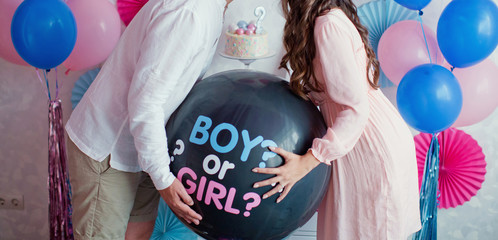 man and woman holding black balloon with "boy or girl?" on gender reveal party