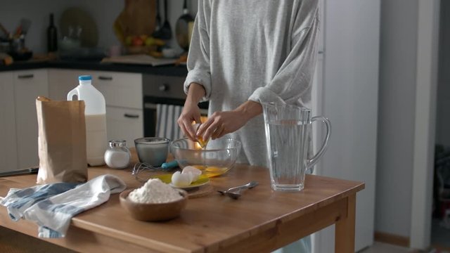Medium shot of young attractive woman standing at kitchen table and cooking breakfast