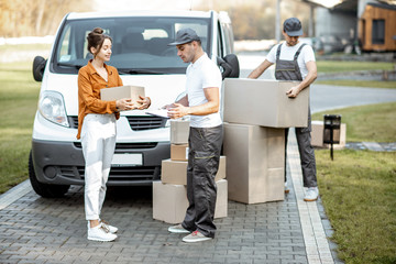 Courier with checklist delivering goods to a young woman by cargo van vehicle, mover with cardboard...