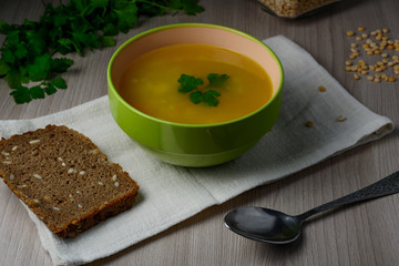 Pea soup with bread and parsley on light wooden table.