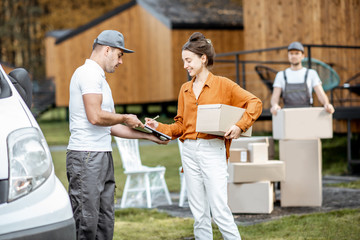 Couriers delivering goods to a young woman home by cargo van vehicle, client signing documents,...