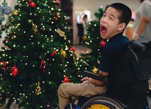 Disabled Child On Wheelchair With Blurry Lights And Decorations On The Christmas Tree, Special Children's Lifestyle, Life In The Education Age Of Special Need Kids, Happy Disability Kid Concept.