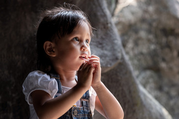 Asian little girl standing in the little cave and she pray and looking up to the light, concept of hope, belief and inspiration in the life.