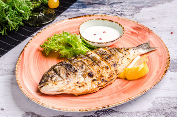 Restaurant food - whole grilled dorado with lemon slices and green beans on platter, restaurant table. Top view baked fish