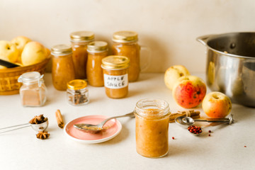 Freshly cooked homemade applesauce in glass jars, ingredients, plate and spoon on kitchen table