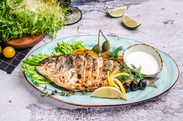 Grilled fish on wooden board with sauce and Provencal herbs, salt, olive oil, spices, cherry tomato on black table background. Top view for menu. Copy space. Healthy eating concept.