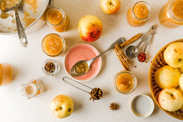 Fresh homemade applesauce in glass jars, plate, utensils, ingredients on kitchen table
