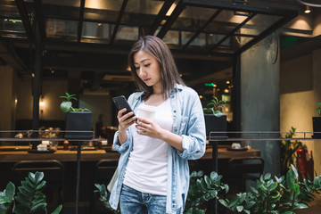 Asian woman browsing on cellphone on street with coffee