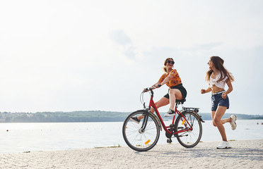 Girl runs near bicycle. Two female friends on the bike have fun at beach near the lake