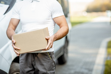 Delivery man holding carboard parcel outdoors, close-up on the box with blank space