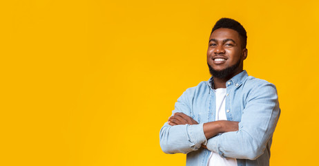 Attractive black guy with folded arms over yellow background - obrazy, fototapety, plakaty