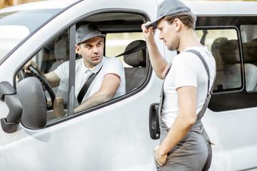 Delivery company employees in uniform delivering goods by cargo van vehicle, mover talking with a...