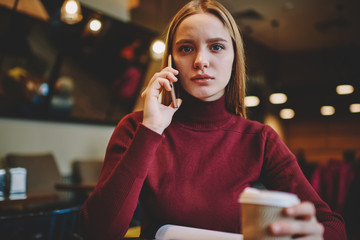 Half length portrait of beautiful confident female person communicating with friends via application on cellphone connected to 4G.Young blonde woman looking at camera while talking on smartphone