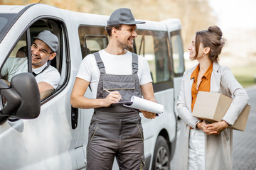 Delivery company employees in uniform delivering goods to a client by cargo van vehicle, woman...