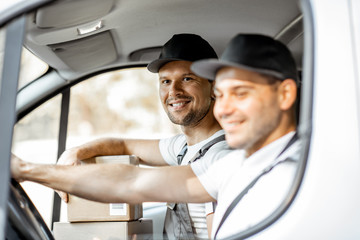 Two cheerful delivery company employees in uniform having fun while driving a cargo vehicle, delivering goods to the customers