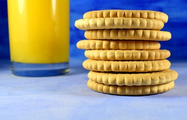 stack of cookies and orange juice in a glass on a blue background