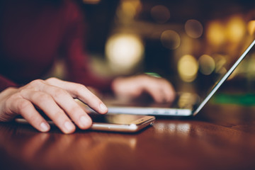 Selective focus on woman's hand putting modern smartphone on wooden table while spending time in coffee shop.Close up blurred image of female fingers touching mobile phone screen during work indoors