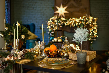 A large table is decorated for the festive dinner and Christmas. Christmas, a big star glows brightly near the fireplace. Loft interior with fireplace decorated for Christmas. Evening photo in warm ti