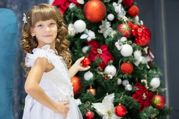 A beautiful child decorates a Christmas tree. Elegant girl in christmas time.