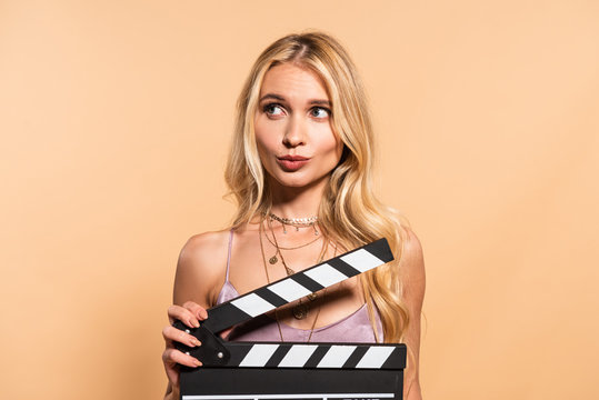 blonde woman in violet satin dress with movie clapper board looking away on beige background