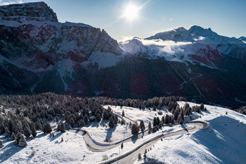 Curved road with car in the Italian Alps in South Tyrol, during winter / Sunny winter day with harsh shadows and lot of snow