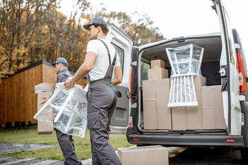 Delivery company employees unloading cargo van vehicle, delivering some goods and furniture to a...