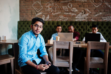 Group of four south asian men's posed at business meeting in cafe. Indians work with laptops together using various gadgets, having conversation. Indian man with mobile phone.