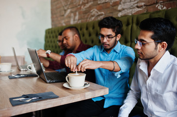 Group of four south asian men's posed at business meeting in cafe. Indians work with laptops together using various gadgets, having conversation and drink coffee.