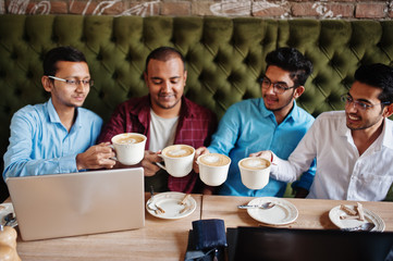 Group of four south asian men's posed at business meeting in cafe. Indians work with laptops together using various gadgets, having conversation and drink coffee.