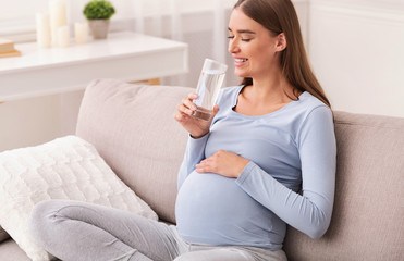 Obraz na płótnie Canvas Positive Pregnant Girl Drinking Water Sitting On Couch At Home