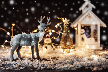 Christmas and New Year holydays composition. Christmas tree, deer and decorations on dark background with light and snow, shallow depth of field